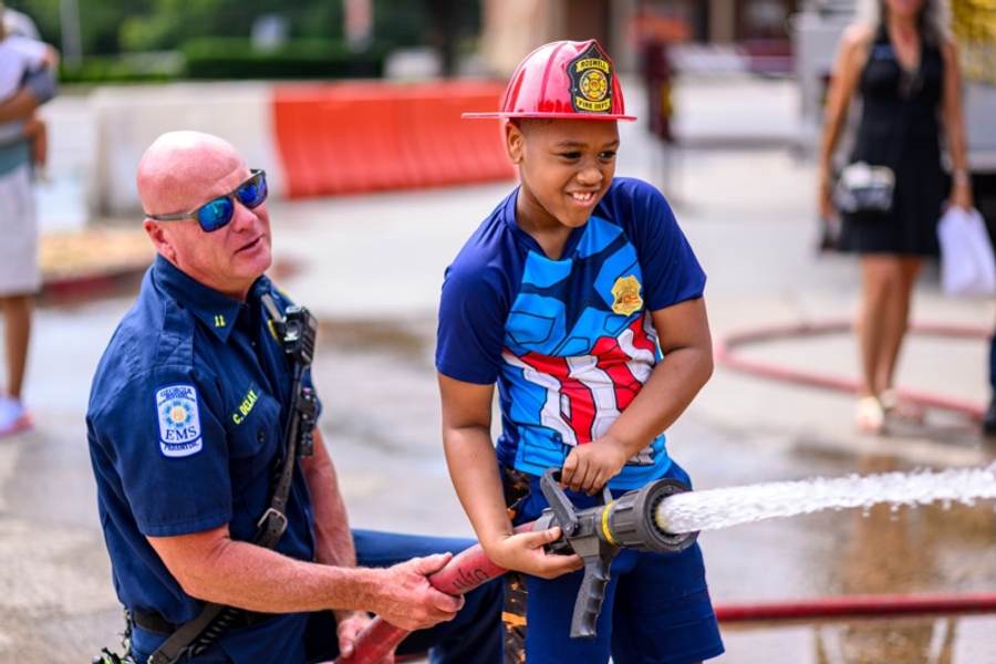 A child grins beneath a charged Roswell Fire hose at an RFRF community event.
